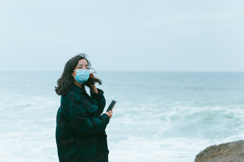 woman in face masks stands in front of ocean view