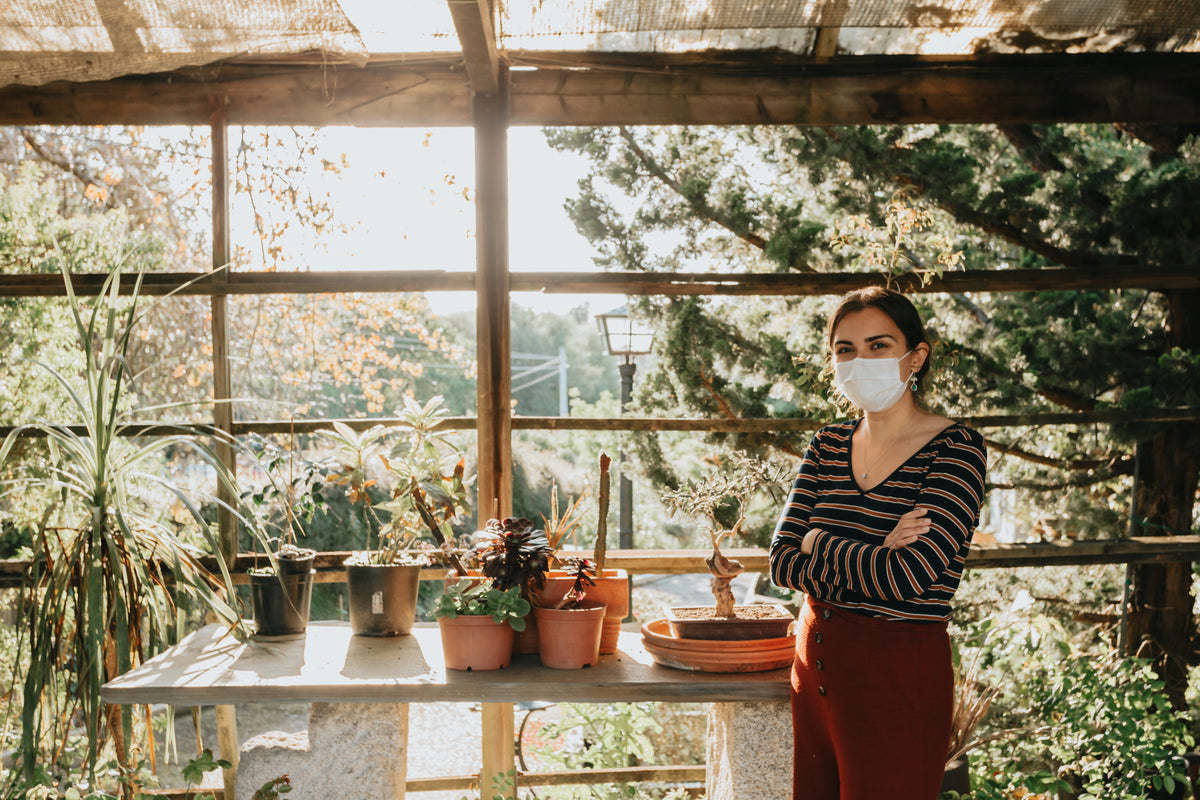 woman in facemask next to potted plants on table