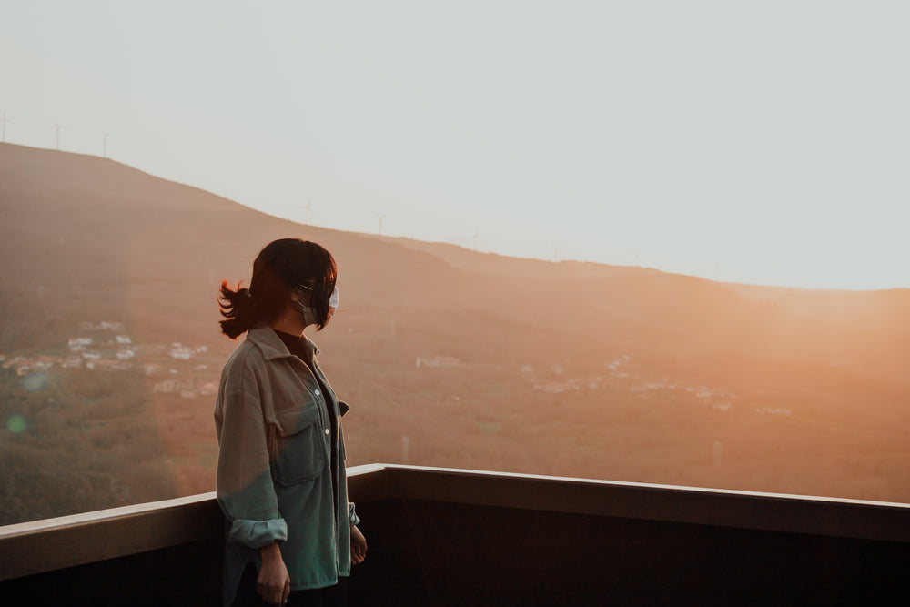 woman in facemask stands bathed in golden light