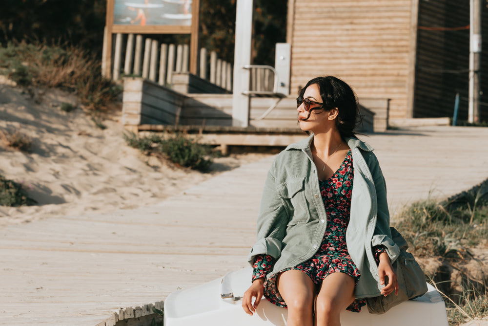 woman in floral dress sits by a wooden boardwalk