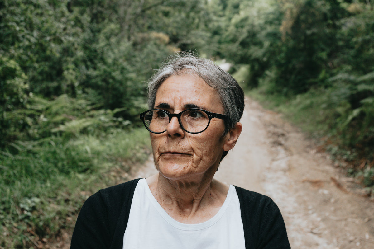 woman in glasses looks left on a green lined dirt trail