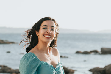 woman in glasses smiles by the rocky shoreline