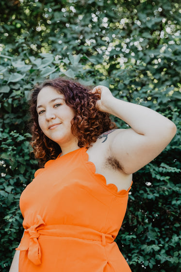 woman in orange top by green plant