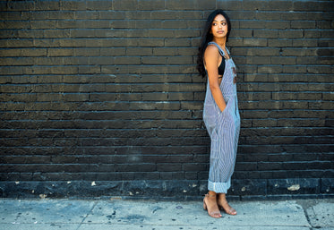 woman in overalls poses by brick wall