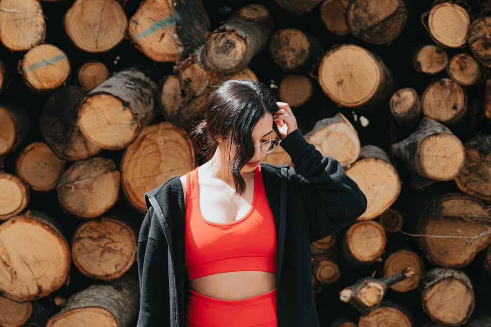 woman in red athletic wear stands in front of a stack of wood