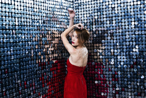 woman in red dress stretches out arms against a wall of mirrors