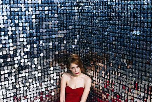 woman in red sits in corner against walls of mirrors