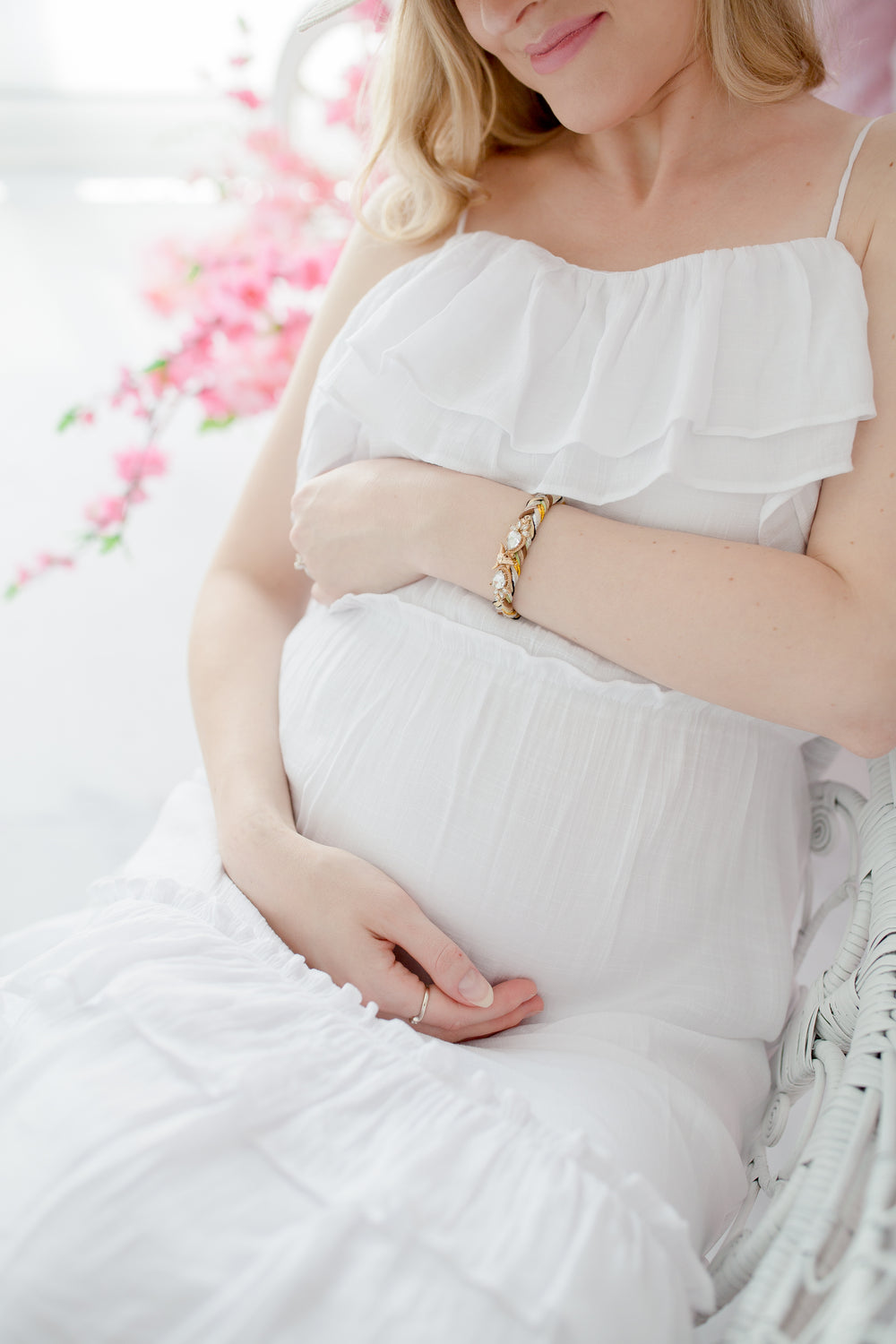 woman in soft white dress sits and holds her pregnant belly