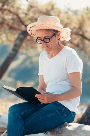 woman in straw hat on a wooden log reading a book