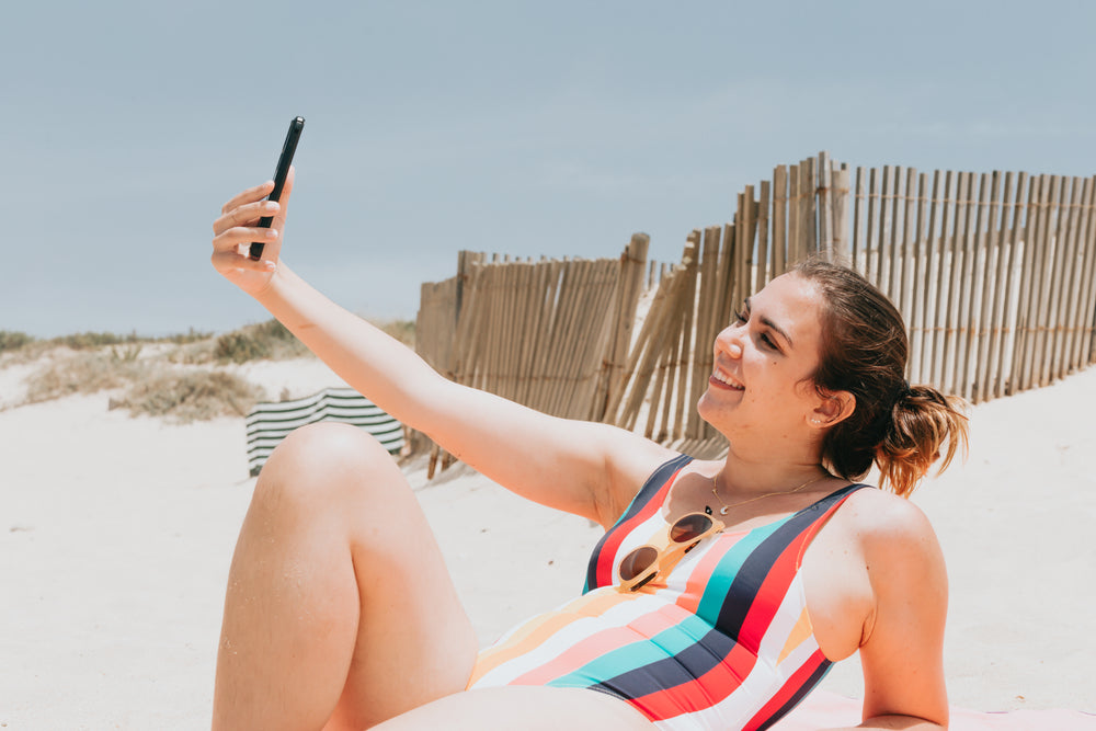 woman in striped bathing suit takes a beach selfie