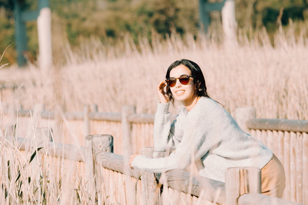 woman in sunglasses leans on a wooden fence