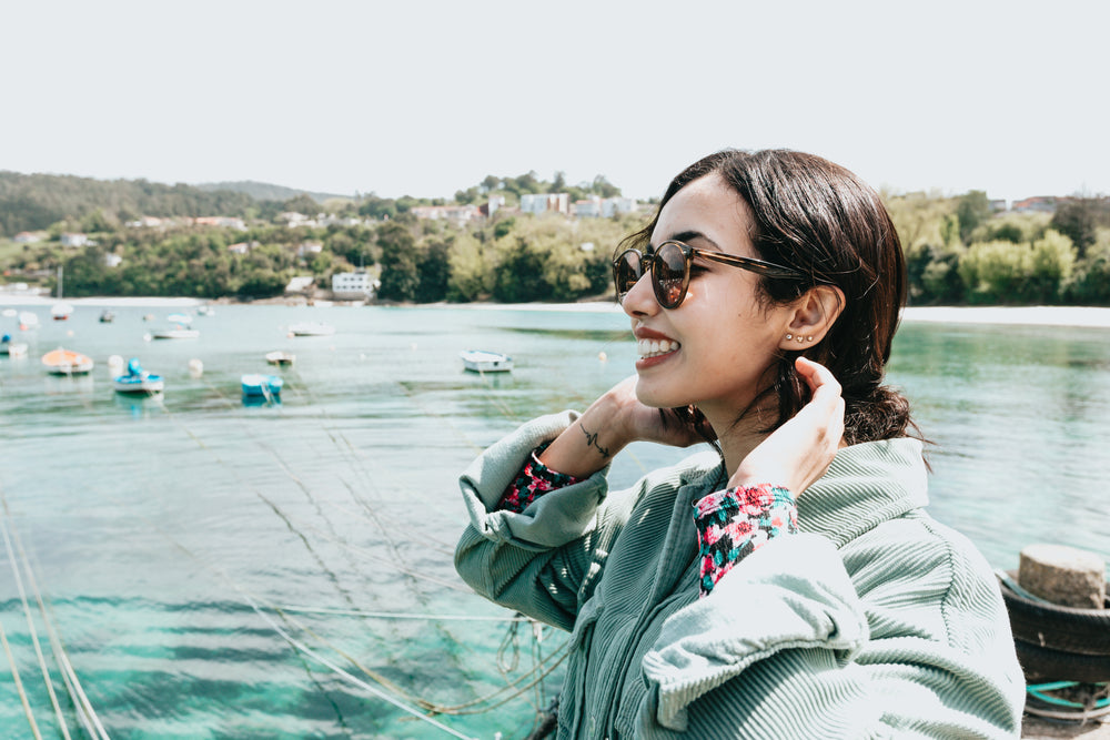 woman in sunglasses pulls hair back and smiles wide