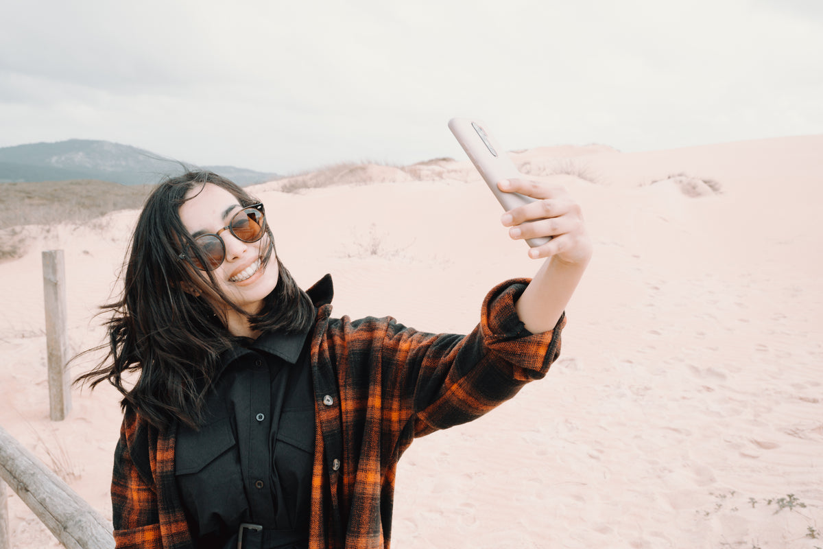 woman in sunglasses takes a selfie at the beach