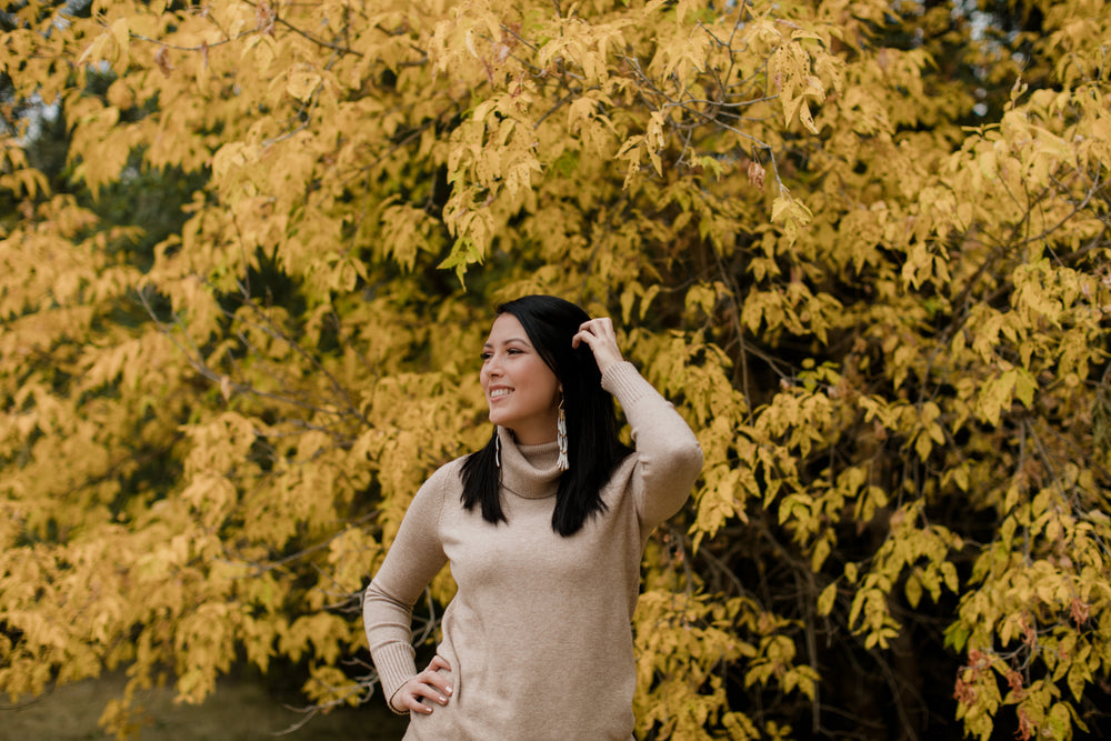 woman in tan sweater smiles standing against yellow trees