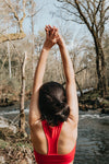 woman in vibrant red reaches arms up in a stretch outdoors
