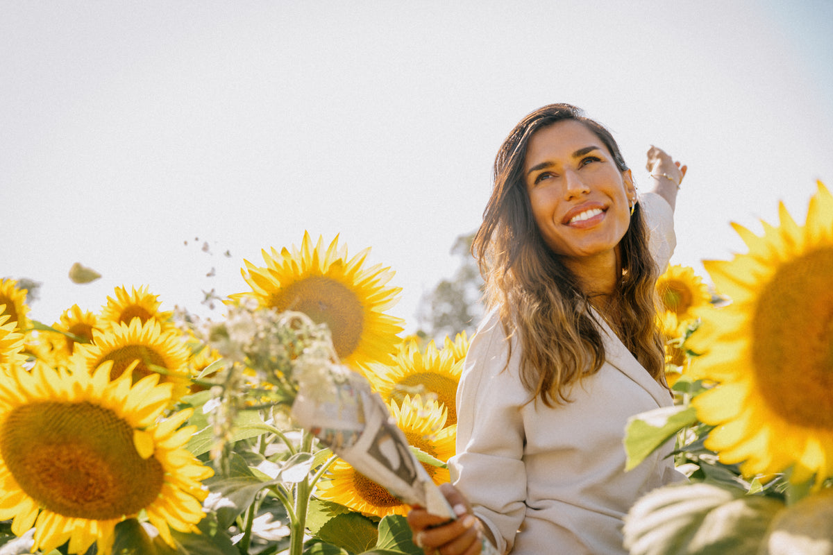 woman in white jacket smiles surrounded by sunflowers