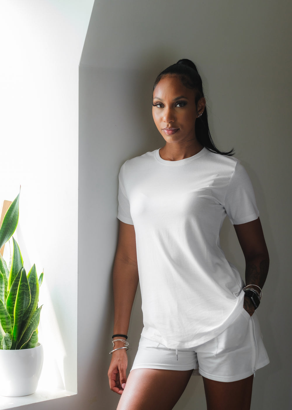 woman in white leans against a wall facing lens