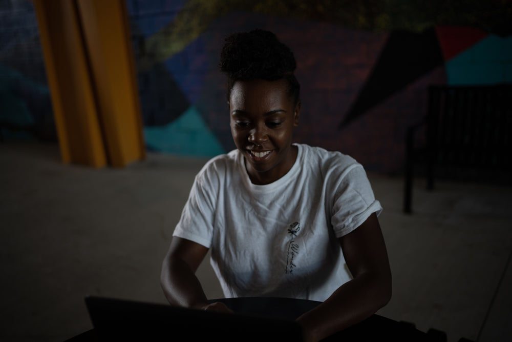 woman in white shirt sits at a table looking at computer