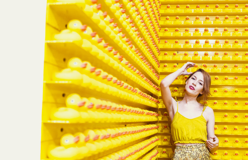 woman in yellow stands before a wall of rubber ducks