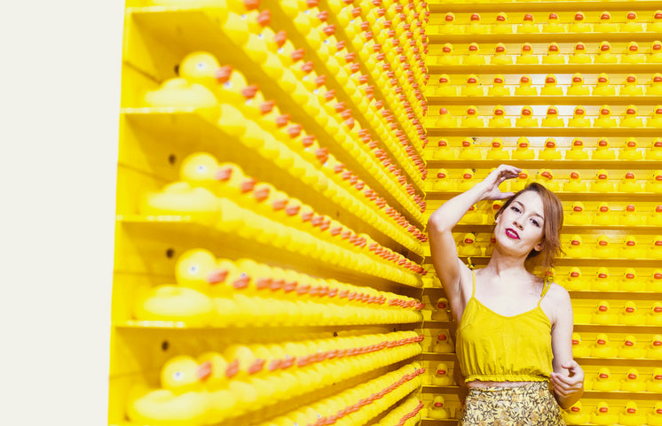 Woman In Yellow Stands Before A Wall Of Rubber Ducks