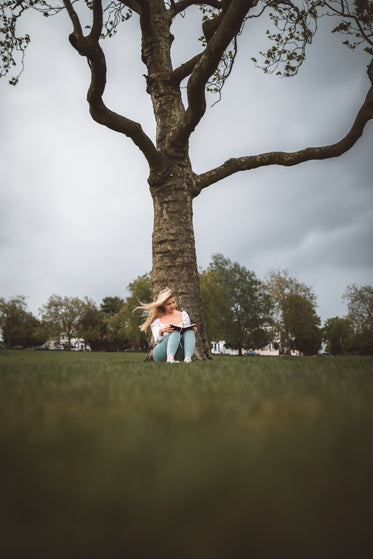 woman is sitting under a tree reading on a breezy day