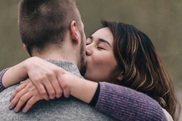 woman kisses man with her arms around his neck