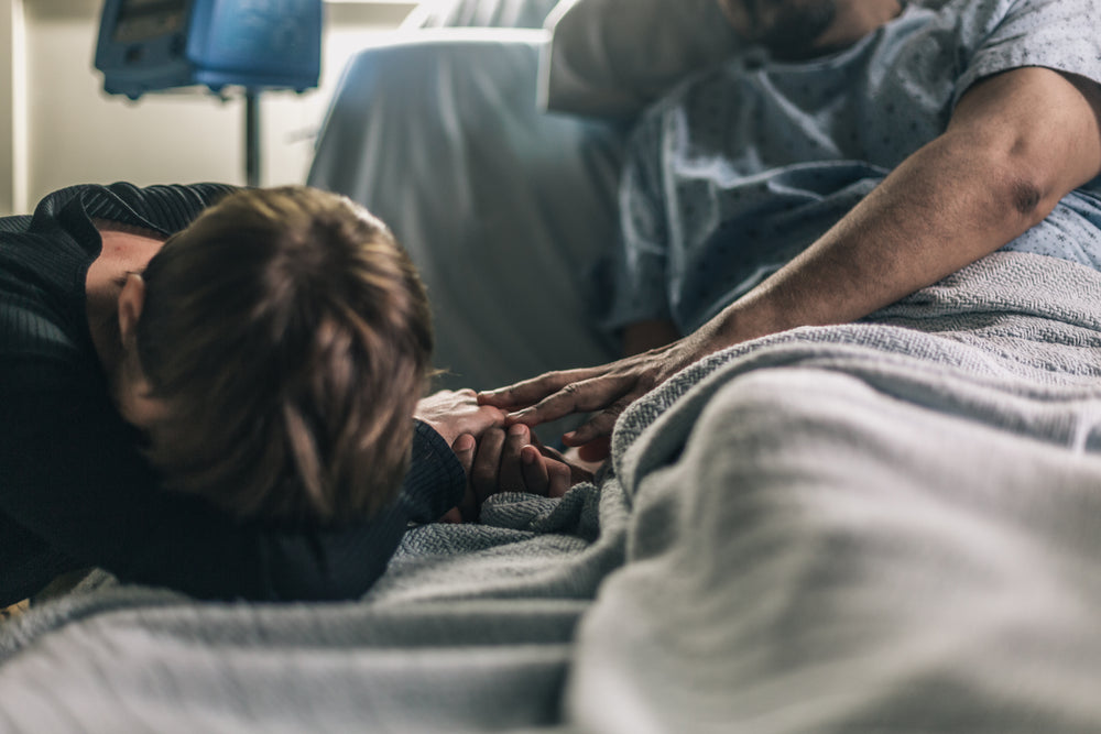 woman lays head on hospital bed while patient comforts her