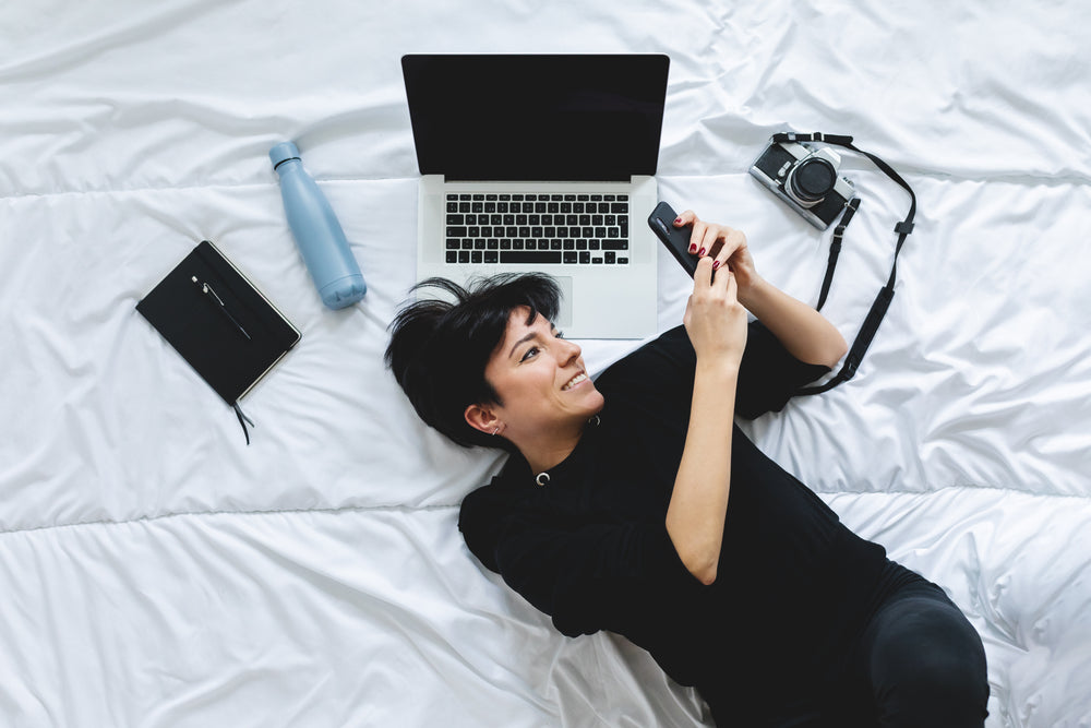 woman lays on a duvet and looks at their cell phone