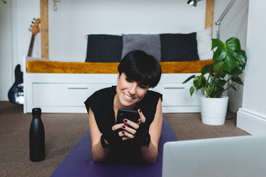 woman lays on a purple yoga mat looking at her phone