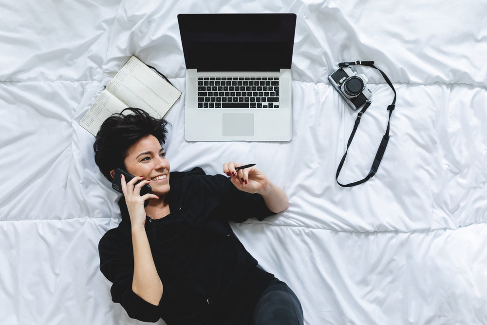 woman lays on her bed while talking on the cell phone