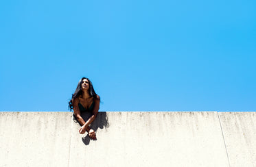 woman leans over city wall with blue sky
