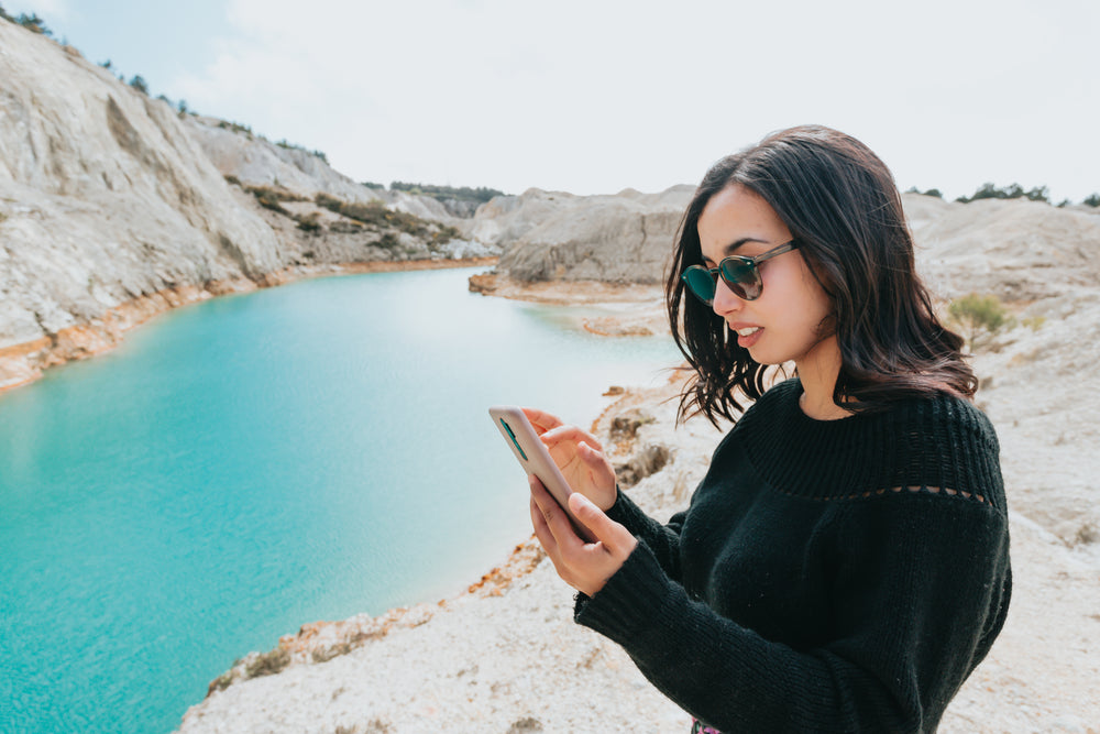 woman looks at her cellphone while by blue water