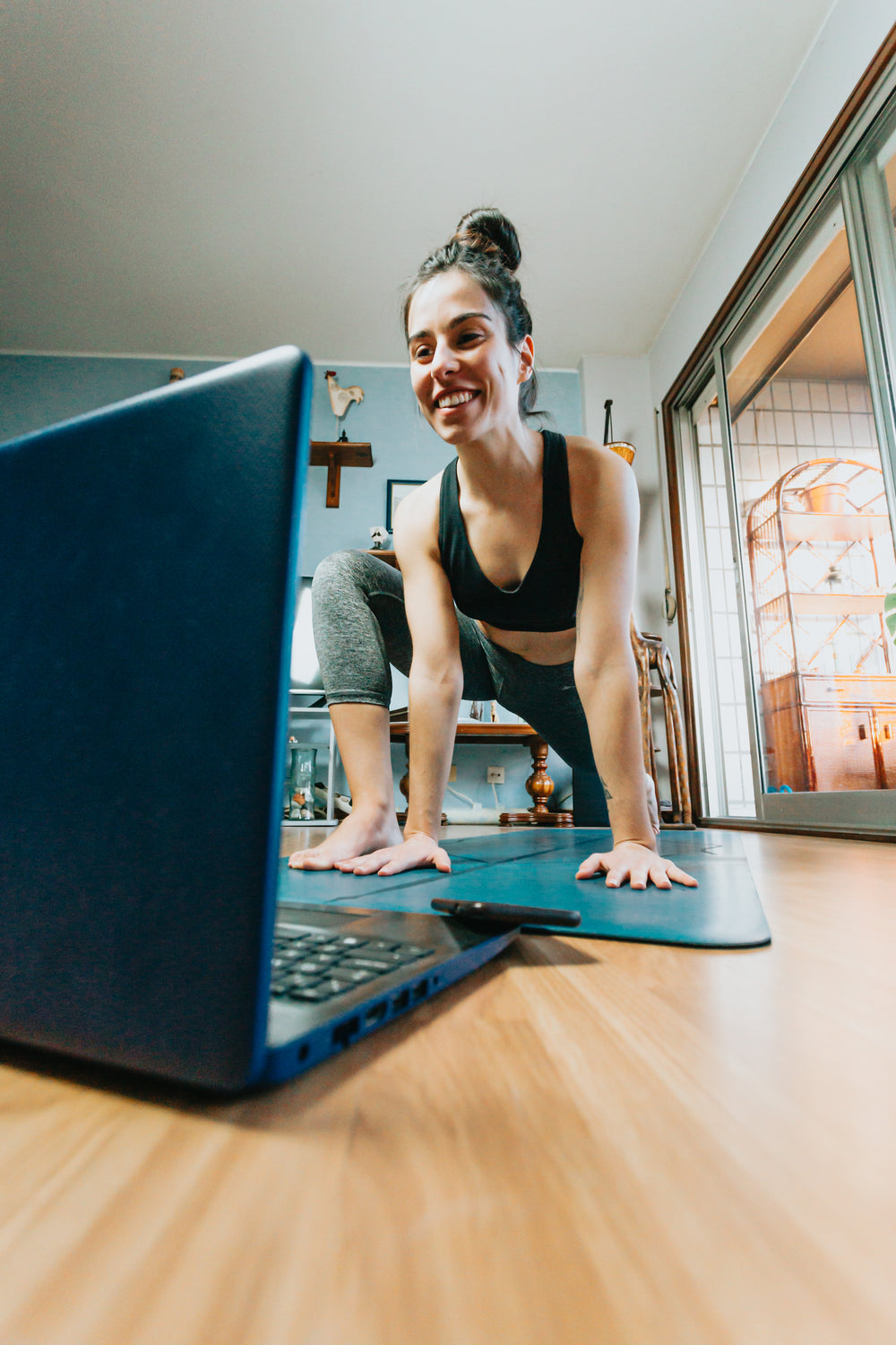 woman looks at open laptop while on blue yoga mat