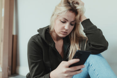 woman looks down at her phone and cradles her head