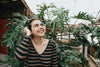 woman looks up and smiles by a large green plant