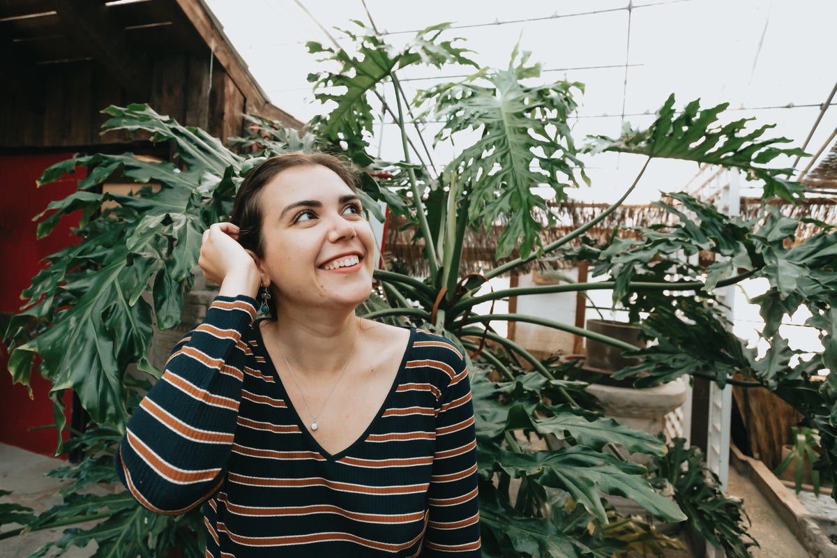 woman looks up and smiles by a large green plant