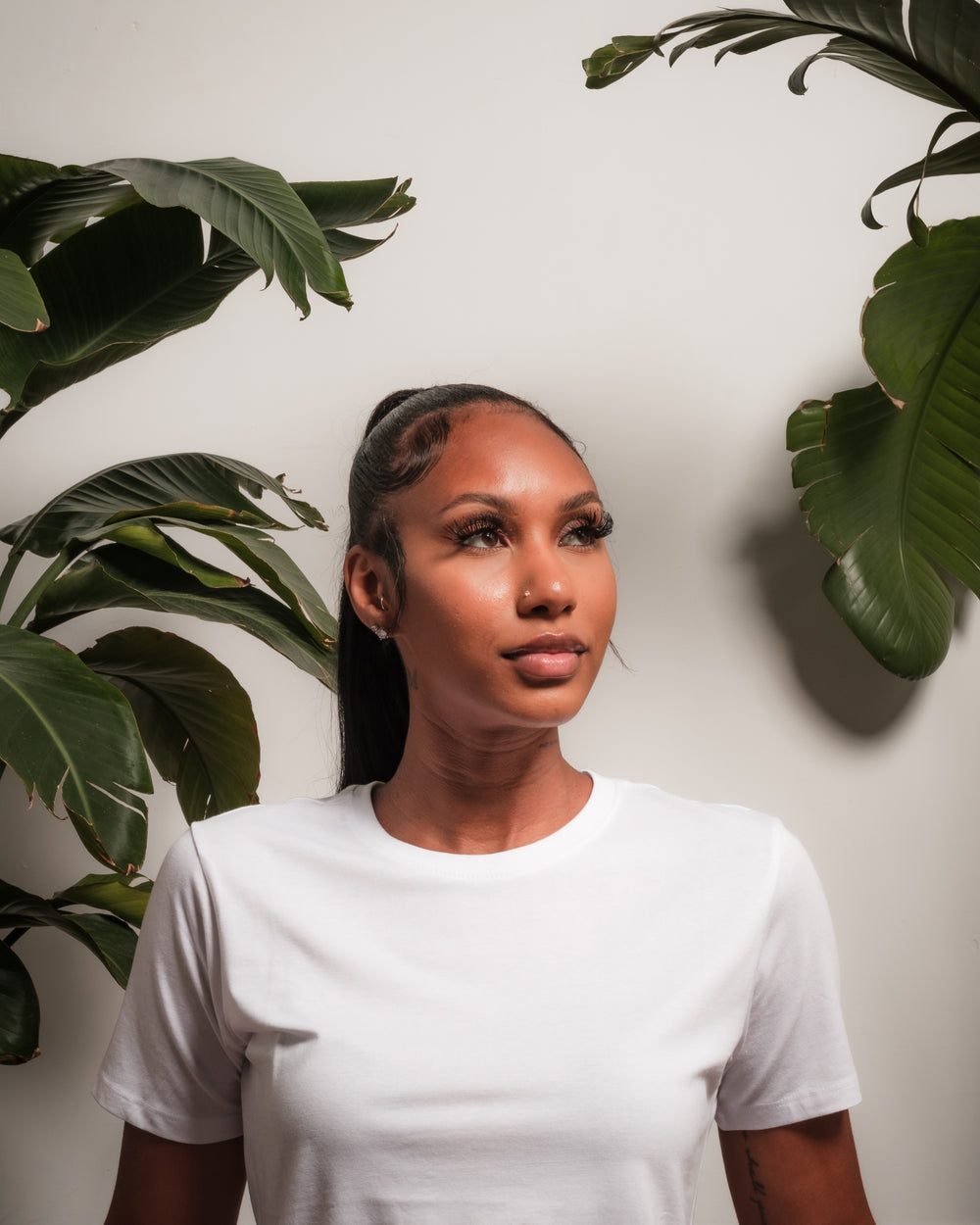 woman looks up to the right in front of a plant lined wall