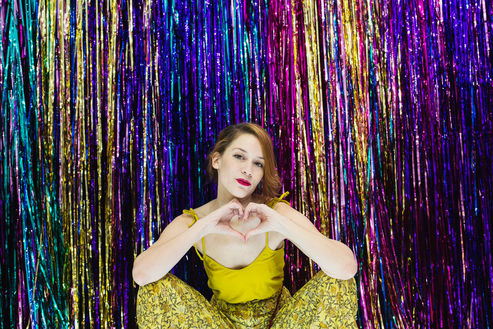 woman makes hand heart gesture in front of rainbow wall