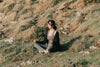 woman meditates outdoors on a green grassy hill