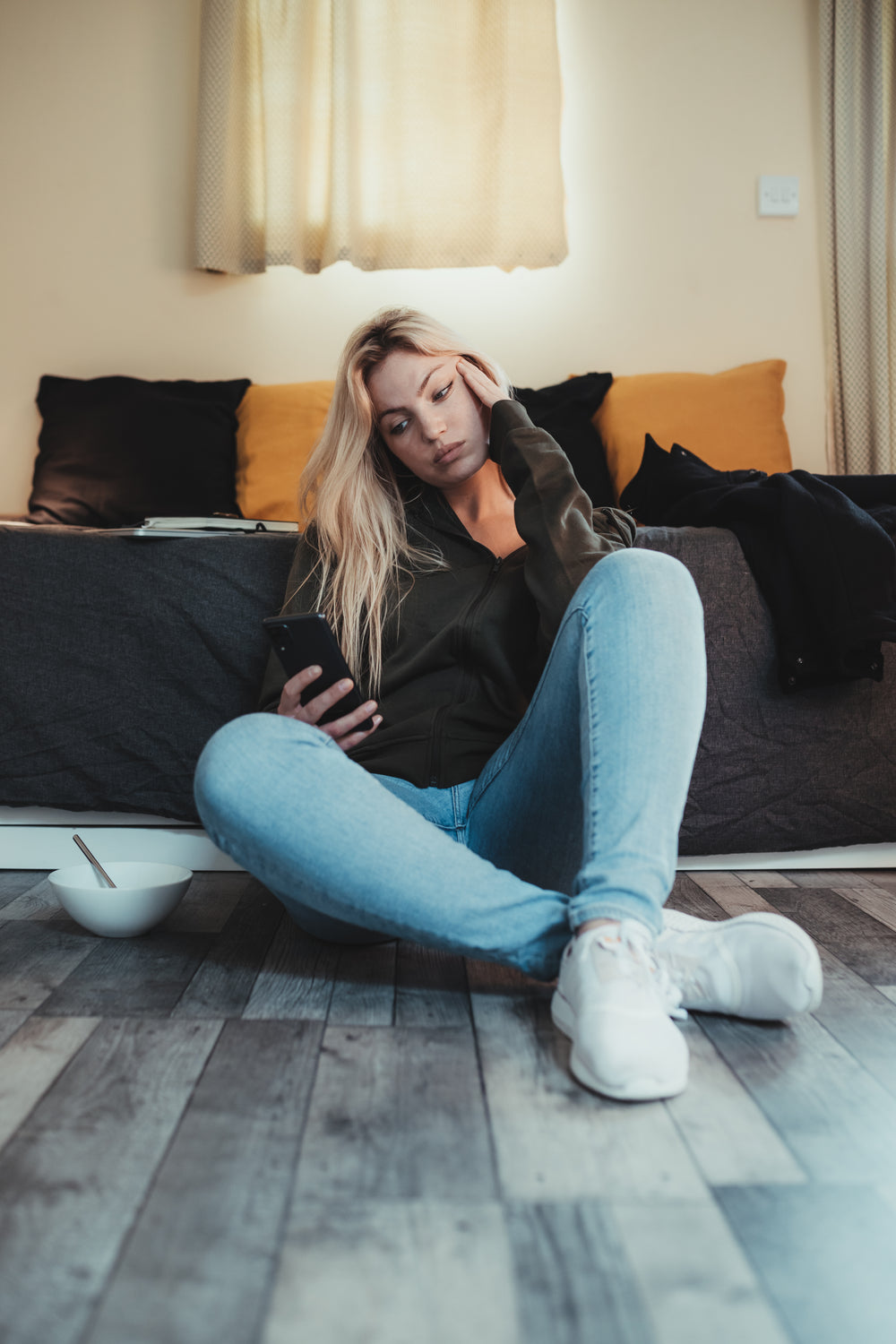 woman on the floor holds her head and her cellphone