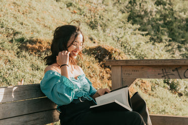 woman outdoors smiles while reading outdoors