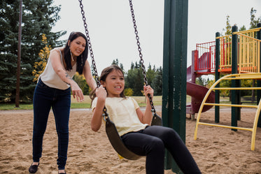 woman plays with child on swing set