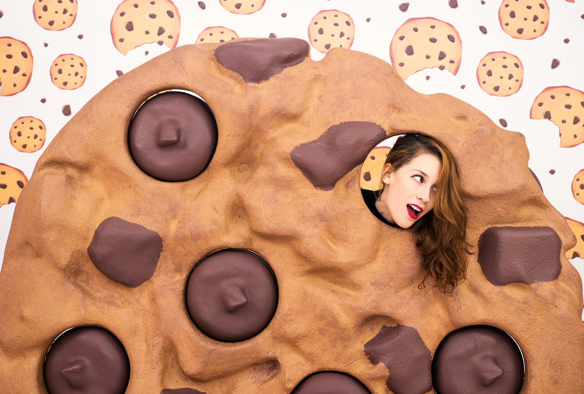 woman pokes her head through a hole in a giant cookie