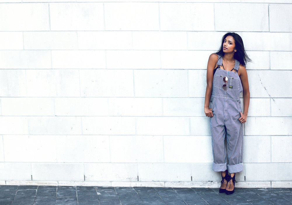 woman poses by brick wall in overalls