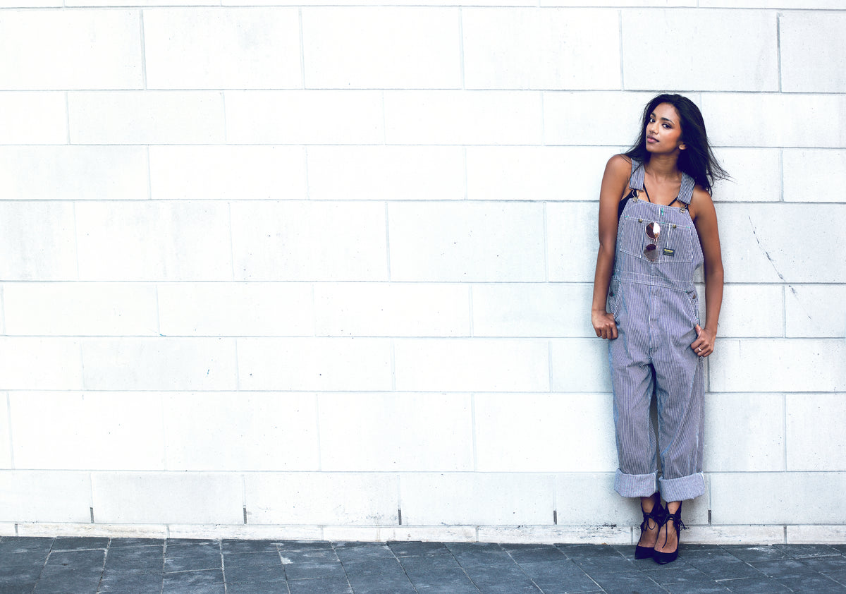 woman poses by brick wall in overalls
