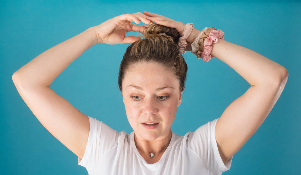 woman puts her hair in a high bun with a scrunchie