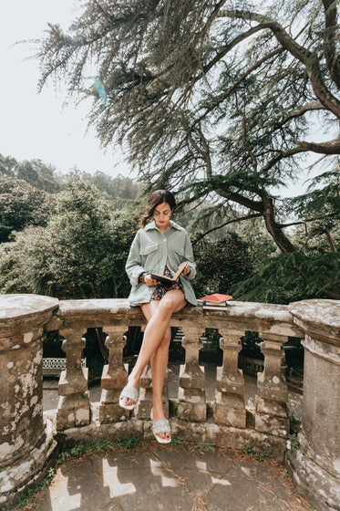 woman reads a book outdoors in front of green leaves