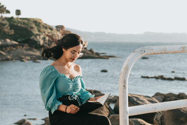 woman reads a book with rocks and water behind her