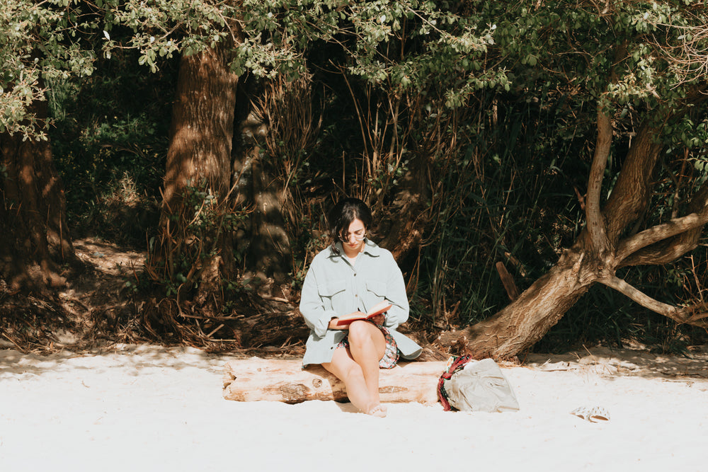 woman reads her book sitting on a wooden log on the beach