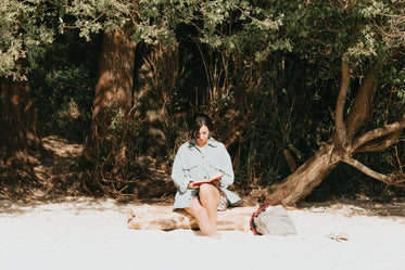 woman reads her book sitting on a wooden log on the beach